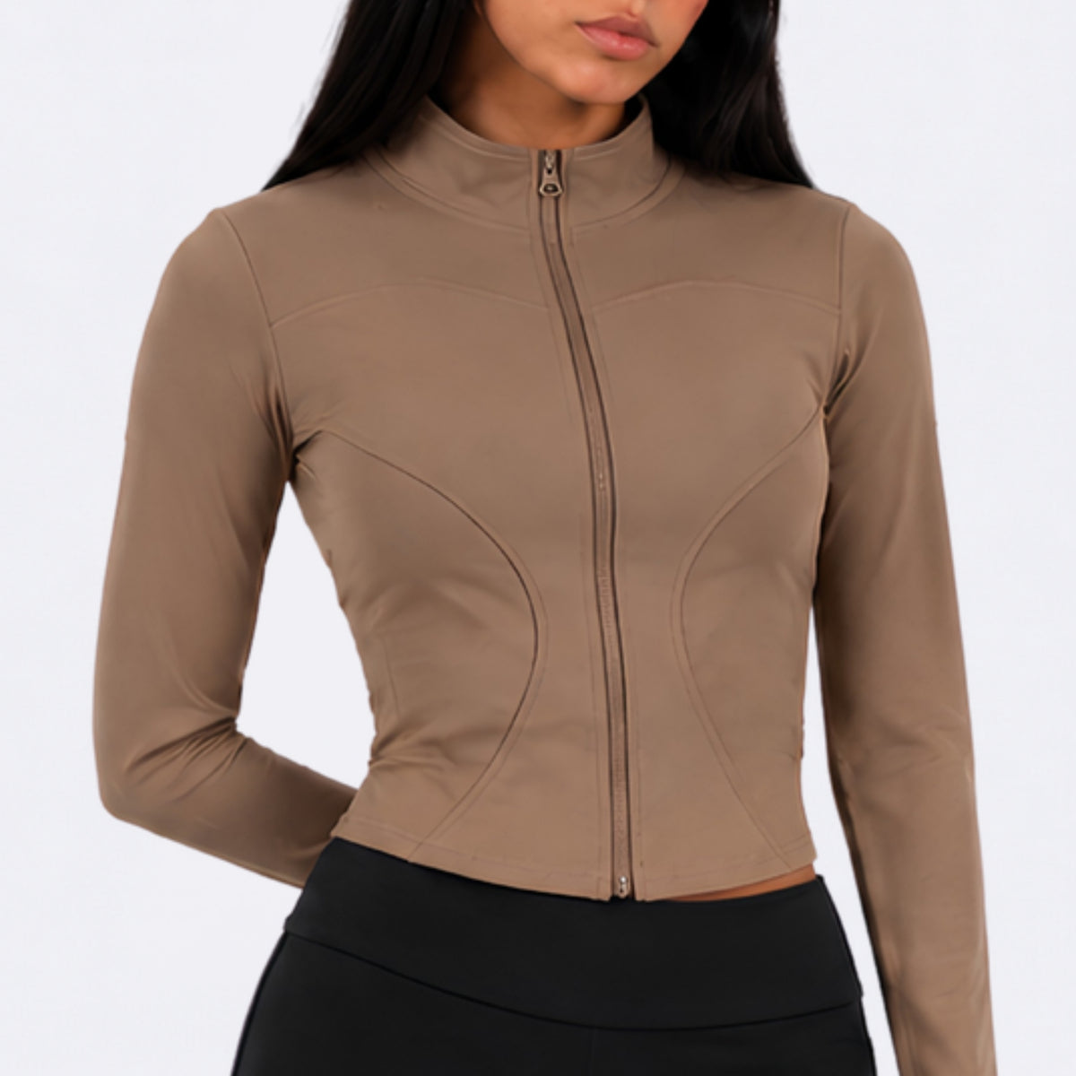 A woman wearing a fitted long-sleeve zip-front top in taupe brown, paired with bottoms, against a plain light studio background.