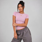 A woman modeling a pink short-sleeve fitted top and pants against a light gray studio background.