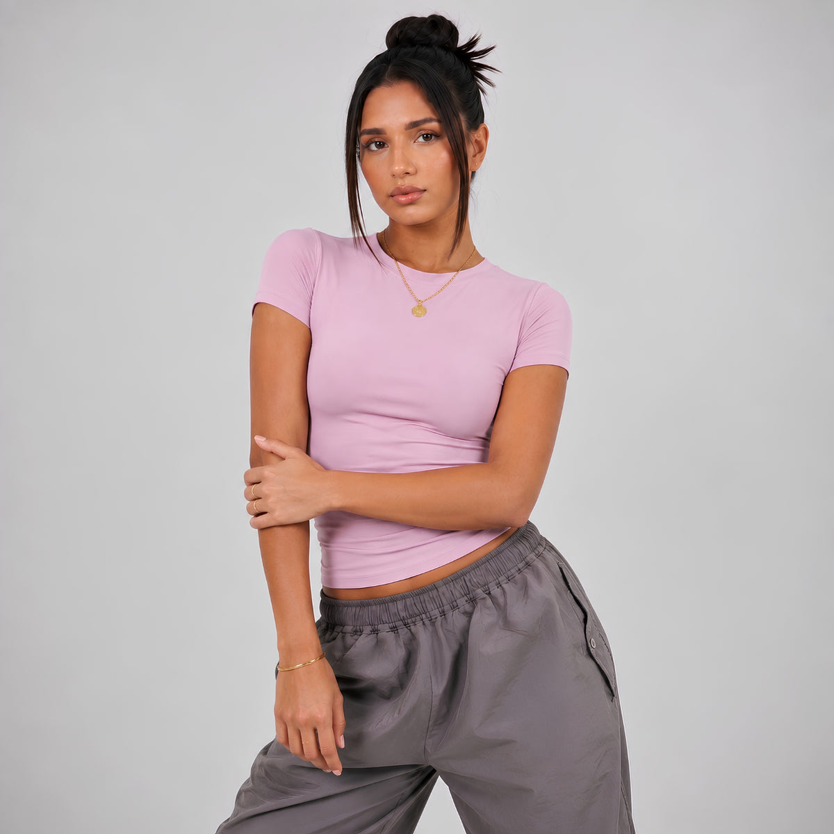 A woman modeling a pink short-sleeve fitted top and pants against a light gray studio background.