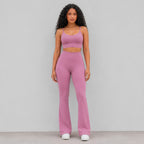 A woman modeling a matching dusty pink activewear set consisting of a sports bra and high-waisted flared leggings, standing against a plain light wall.