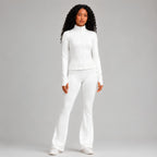 A model wearing a matching white long-sleeve cropped zip-up jacket and high-waisted flared pants, standing against a solid studio background.