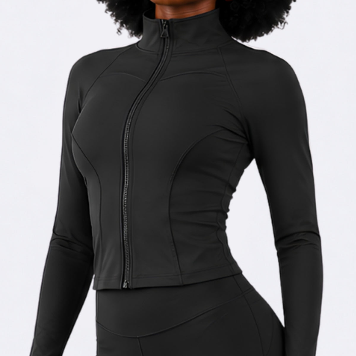 A woman wearing a fitted black long-sleeve athletic top with a high mock neck and front zipper, shown against a plain light studio background.