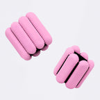 A pair of pink padded wrist and ankle adjustable weighted bands with segmented cylindrical padding and black trim, shown on a clean light gray background.